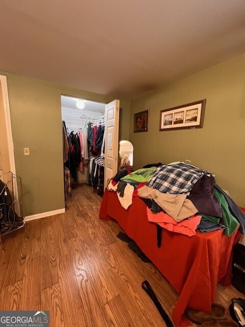 bedroom with a spacious closet, wood finished floors, a closet, and baseboards