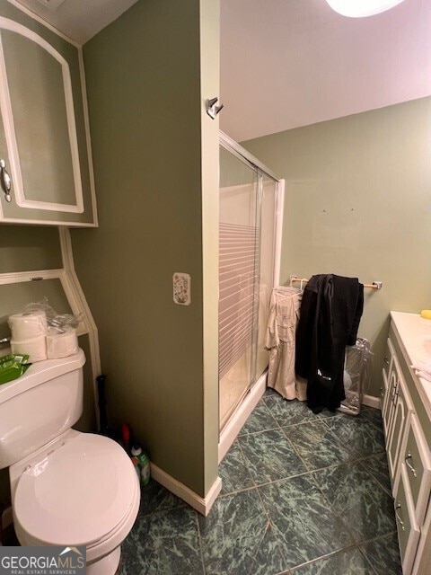 bathroom with toilet, a stall shower, vanity, and baseboards