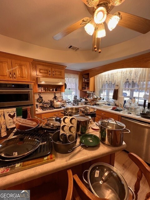 kitchen with visible vents, brown cabinets, under cabinet range hood, stainless steel double oven, and light countertops