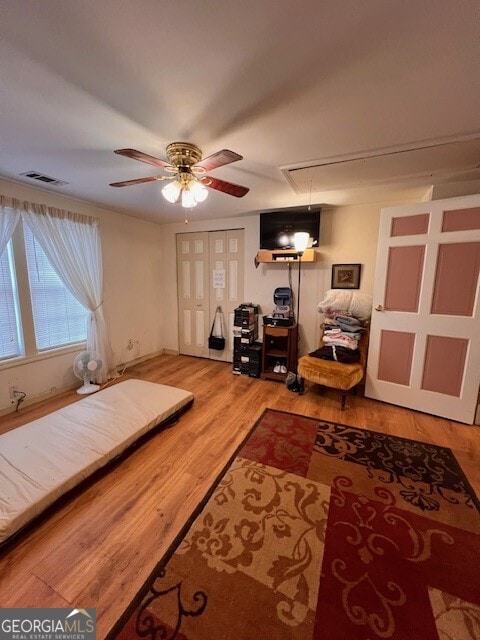 interior space with a ceiling fan, attic access, wood finished floors, and visible vents