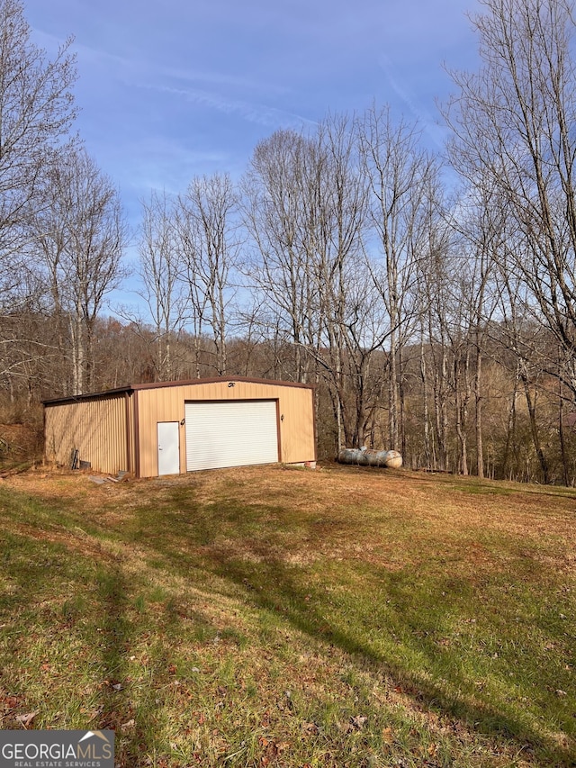 view of yard featuring a forest view, a garage, and an outbuilding