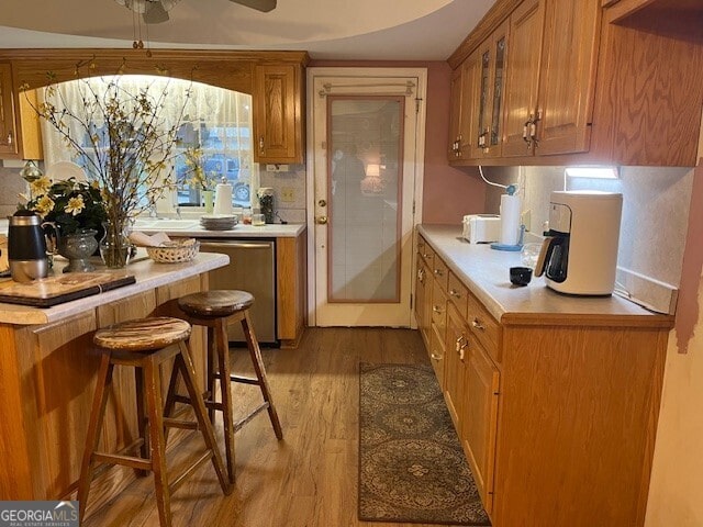 kitchen with brown cabinets, wood finished floors, light countertops, and stainless steel dishwasher