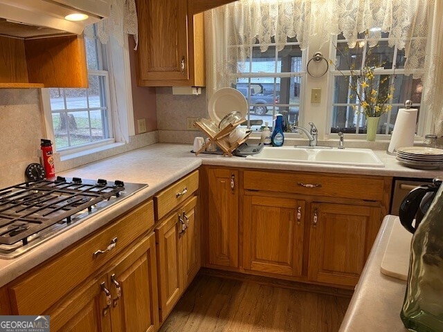 kitchen featuring a sink, wood finished floors, stainless steel gas stovetop, brown cabinetry, and light countertops