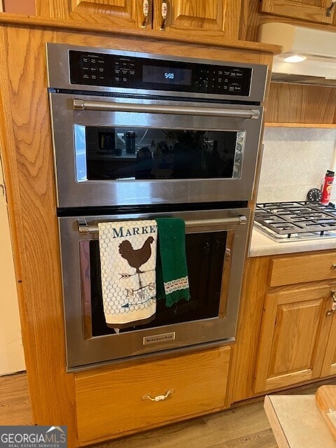 room details featuring backsplash, light countertops, appliances with stainless steel finishes, light wood-style floors, and brown cabinetry