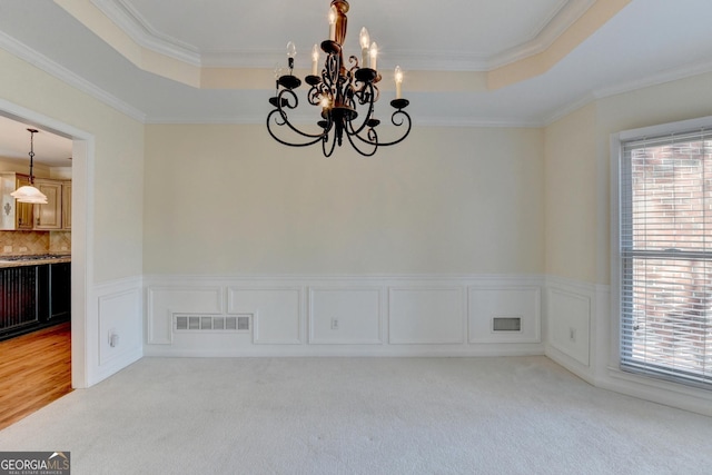 carpeted spare room featuring a chandelier, a raised ceiling, a wealth of natural light, and crown molding