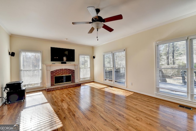 unfurnished living room with a brick fireplace, ornamental molding, ceiling fan, a healthy amount of sunlight, and light hardwood / wood-style flooring