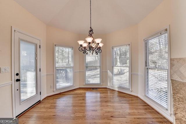 unfurnished dining area with light hardwood / wood-style floors, vaulted ceiling, and an inviting chandelier