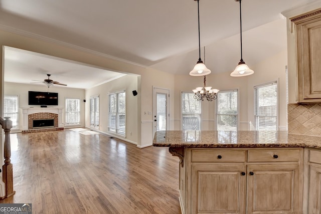 kitchen featuring pendant lighting, ceiling fan with notable chandelier, a brick fireplace, tasteful backsplash, and light stone counters