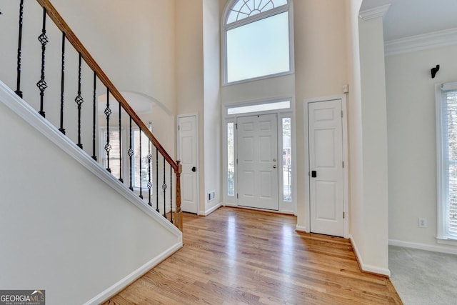 entrance foyer with light wood-type flooring, ornamental molding, a wealth of natural light, and a towering ceiling