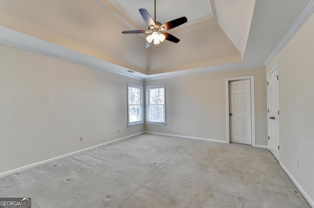 empty room with a tray ceiling, crown molding, ceiling fan, and light colored carpet