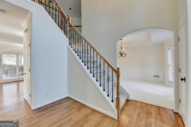 stairs featuring hardwood / wood-style flooring, an inviting chandelier, a tray ceiling, and ornamental molding