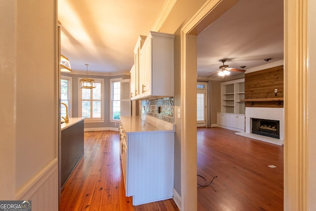 kitchen with built in features, pendant lighting, wood-type flooring, white cabinets, and ornamental molding