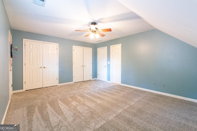 unfurnished bedroom with carpet floors, vaulted ceiling, ceiling fan, and multiple closets