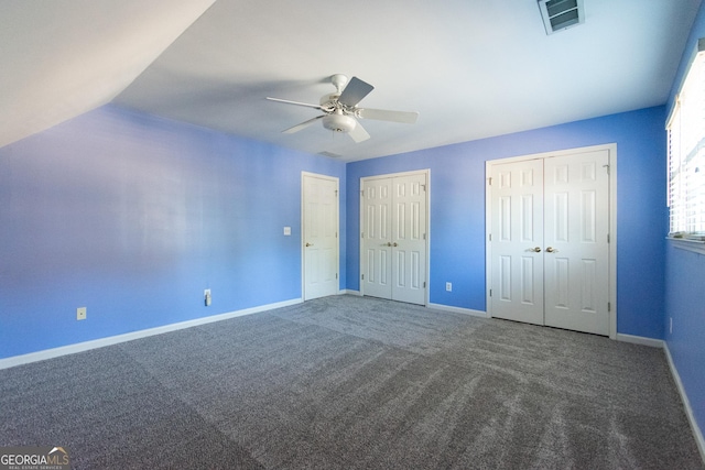 unfurnished bedroom featuring dark colored carpet, ceiling fan, lofted ceiling, and two closets