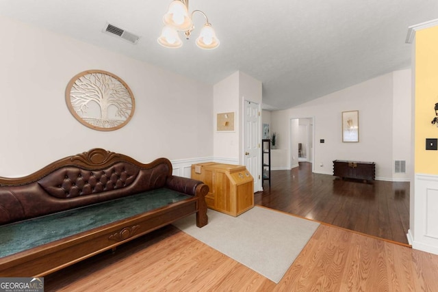 living room with hardwood / wood-style flooring, a notable chandelier, and vaulted ceiling