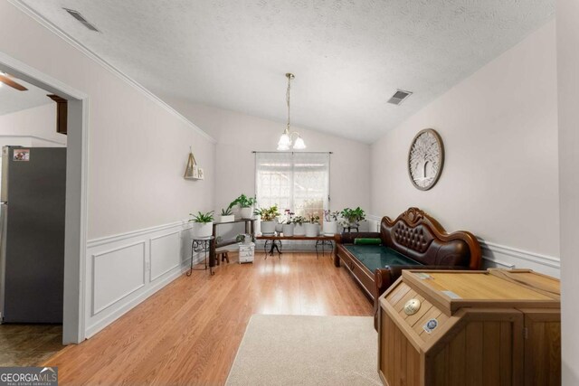 living area with light hardwood / wood-style floors, an inviting chandelier, a textured ceiling, and vaulted ceiling