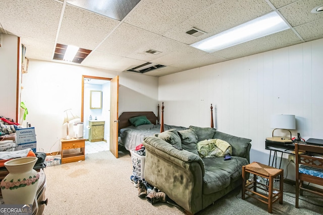 bedroom with connected bathroom, a paneled ceiling, wood walls, and dark carpet