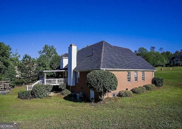 view of side of home featuring a yard, a chimney, roof with shingles, and brick siding
