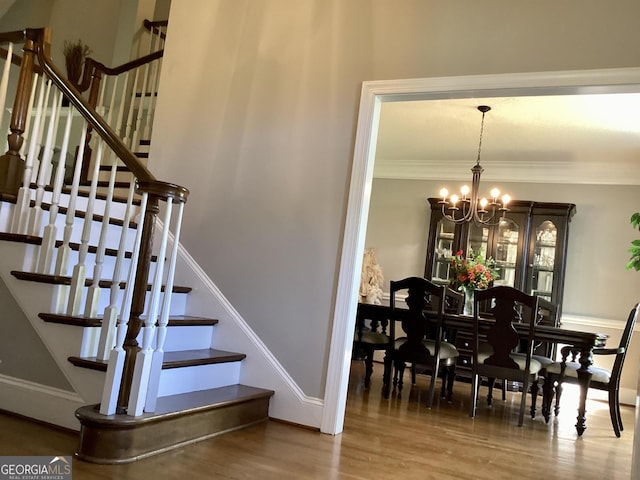 stairs with wood-type flooring, ornamental molding, and a chandelier