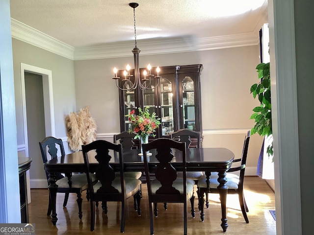 dining room with a textured ceiling, wood-type flooring, crown molding, and a chandelier