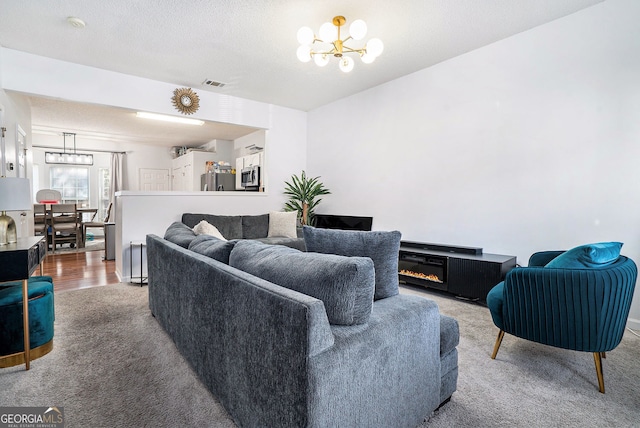 living room with a notable chandelier, visible vents, carpet floors, and a textured ceiling