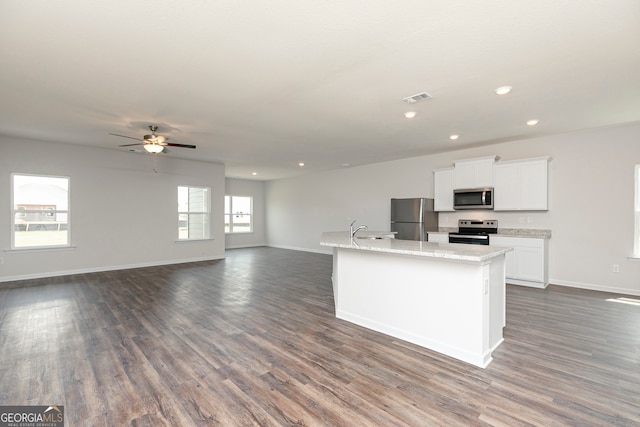 kitchen with dark hardwood / wood-style flooring, light stone counters, stainless steel appliances, a center island with sink, and white cabinetry