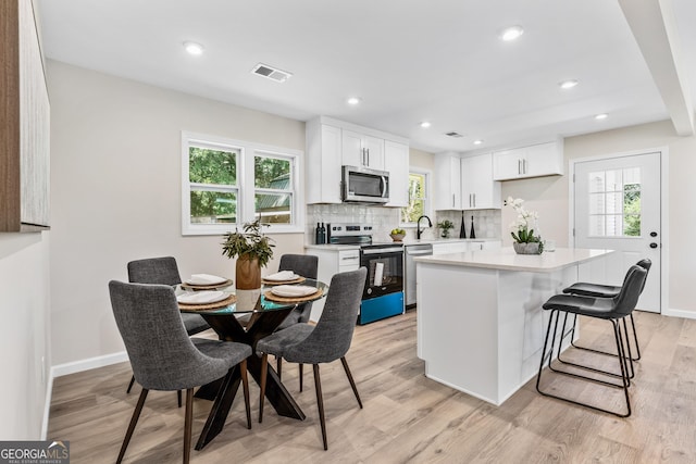 kitchen with plenty of natural light, white cabinets, light wood-type flooring, and appliances with stainless steel finishes