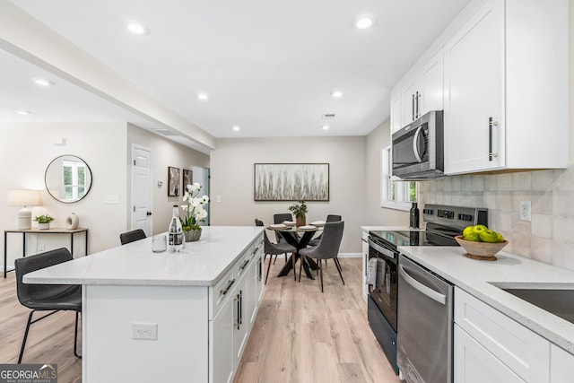 kitchen featuring a breakfast bar, white cabinets, light hardwood / wood-style flooring, appliances with stainless steel finishes, and light stone counters