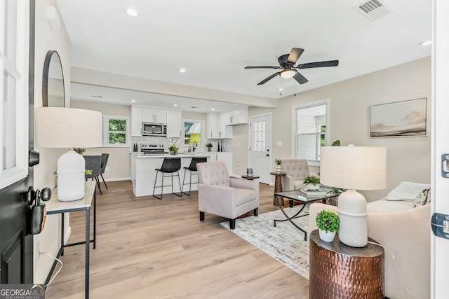 living room with ceiling fan, sink, and light wood-type flooring