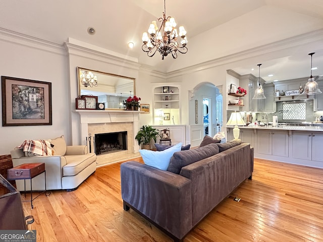 living room with lofted ceiling, a fireplace, an inviting chandelier, light hardwood / wood-style flooring, and built in shelves