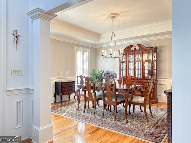 dining area with crown molding, a notable chandelier, hardwood / wood-style flooring, a tray ceiling, and decorative columns