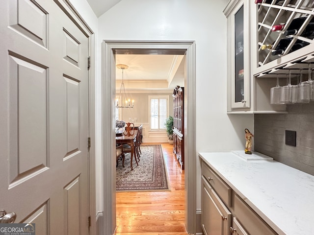 interior space featuring backsplash, a notable chandelier, a tray ceiling, light wood-type flooring, and light stone countertops