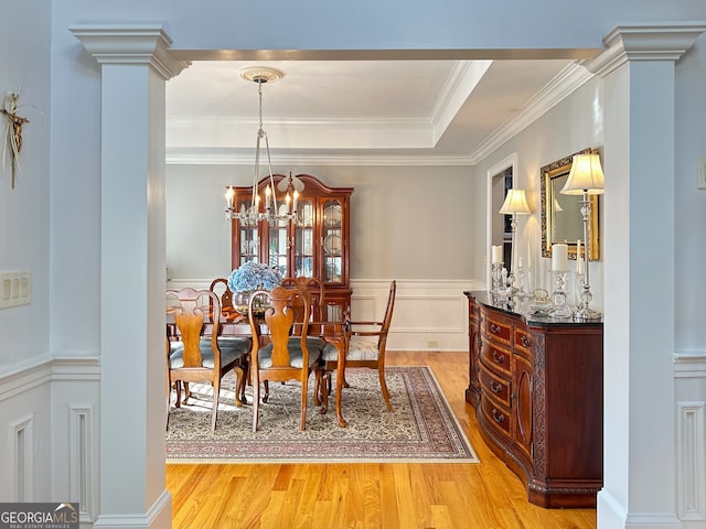 dining area featuring a raised ceiling, ornamental molding, a notable chandelier, and light wood-type flooring