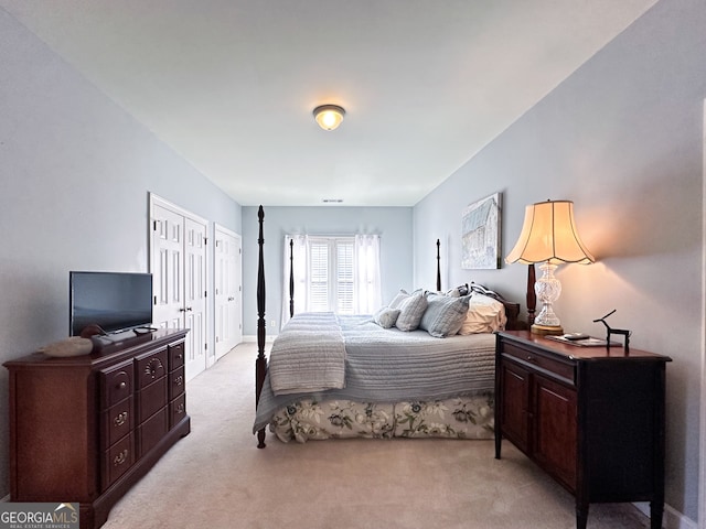 bedroom featuring light carpet and two closets