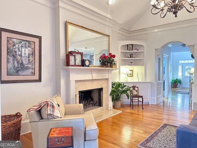 living room with an inviting chandelier, hardwood / wood-style floors, lofted ceiling, a fireplace, and built in shelves