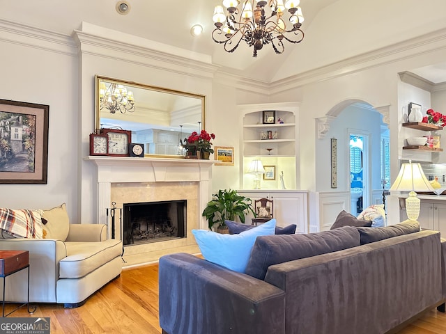 living room with built in shelves, a premium fireplace, light hardwood / wood-style floors, a notable chandelier, and vaulted ceiling