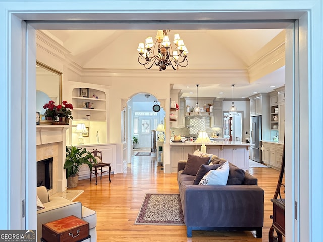 living room featuring lofted ceiling, built in shelves, a premium fireplace, a chandelier, and light wood-type flooring