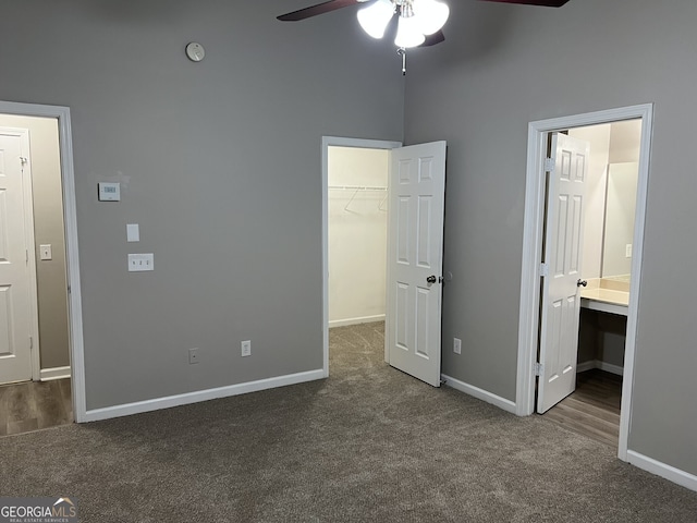 unfurnished bedroom with a walk in closet, ensuite bathroom, ceiling fan, dark colored carpet, and a closet