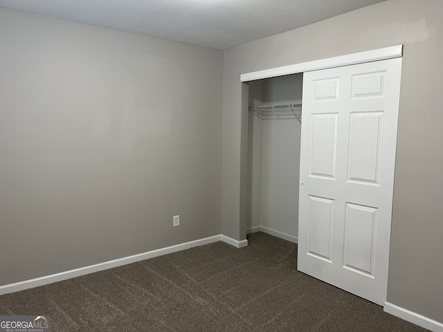 unfurnished bedroom with dark colored carpet and a closet