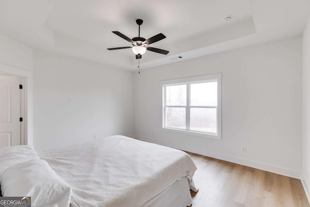 bedroom featuring a tray ceiling, light hardwood / wood-style flooring, and ceiling fan