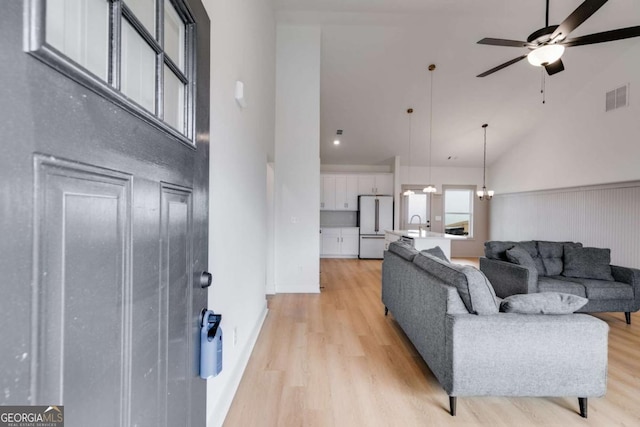 living room featuring ceiling fan with notable chandelier, light hardwood / wood-style floors, and high vaulted ceiling