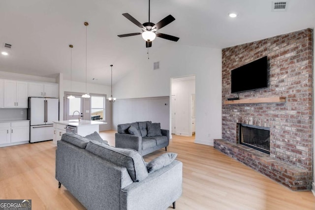 living room with a fireplace, high vaulted ceiling, ceiling fan with notable chandelier, and light wood-type flooring