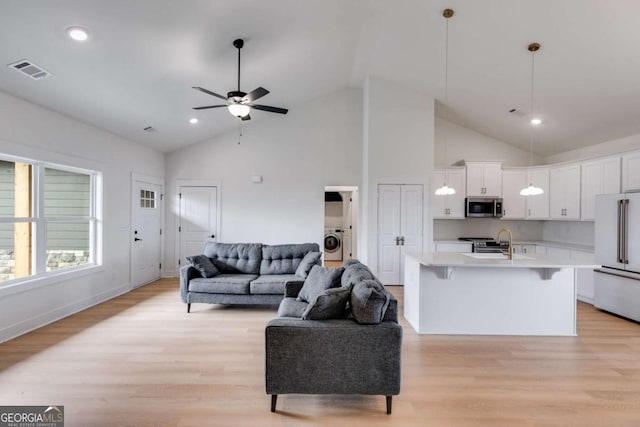 living room featuring washer / clothes dryer, light hardwood / wood-style flooring, ceiling fan, and sink