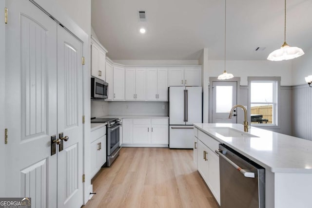 kitchen featuring pendant lighting, sink, an island with sink, white cabinetry, and stainless steel appliances