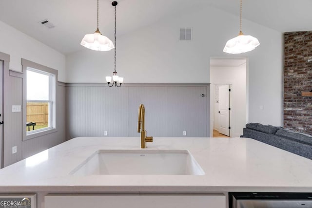 kitchen with light stone countertops, sink, brick wall, pendant lighting, and lofted ceiling