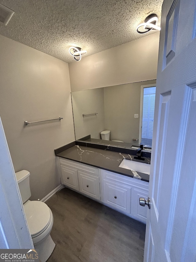 bathroom with hardwood / wood-style floors, vanity, toilet, and a textured ceiling