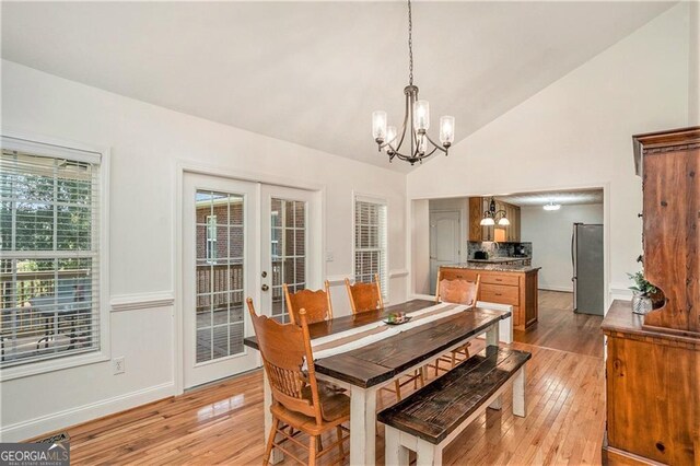 dining space featuring french doors, a chandelier, lofted ceiling, and light wood-type flooring