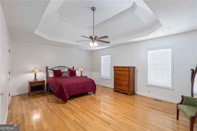 bedroom featuring a raised ceiling, ceiling fan, a textured ceiling, and light wood-type flooring