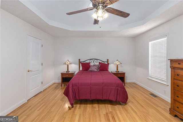 bedroom with ceiling fan, light wood-type flooring, and a tray ceiling