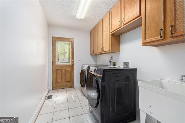 clothes washing area with cabinets, sink, washing machine and dryer, light tile patterned floors, and a textured ceiling